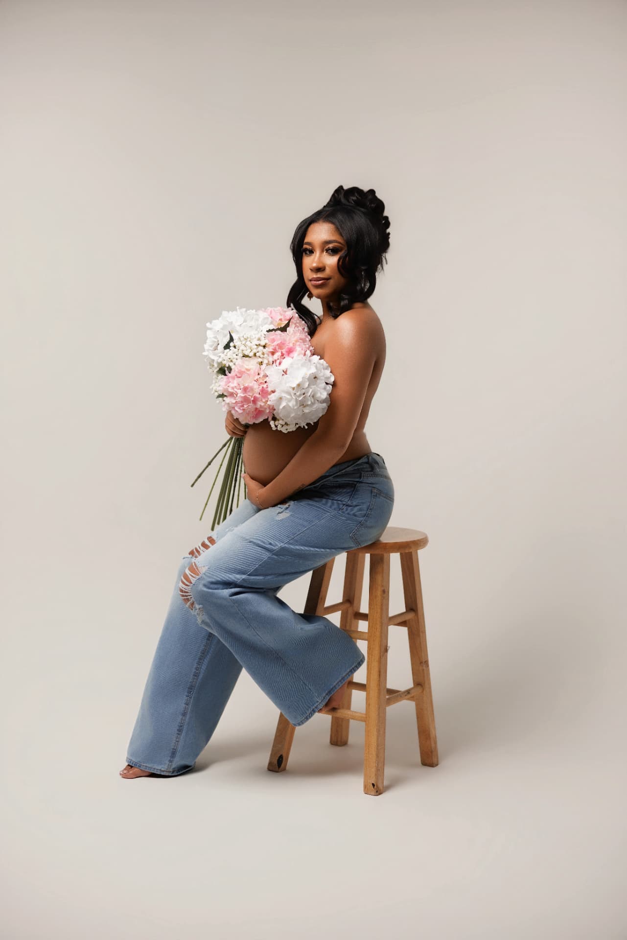 Expectant mother with hydrangeas seated on a wooden stool